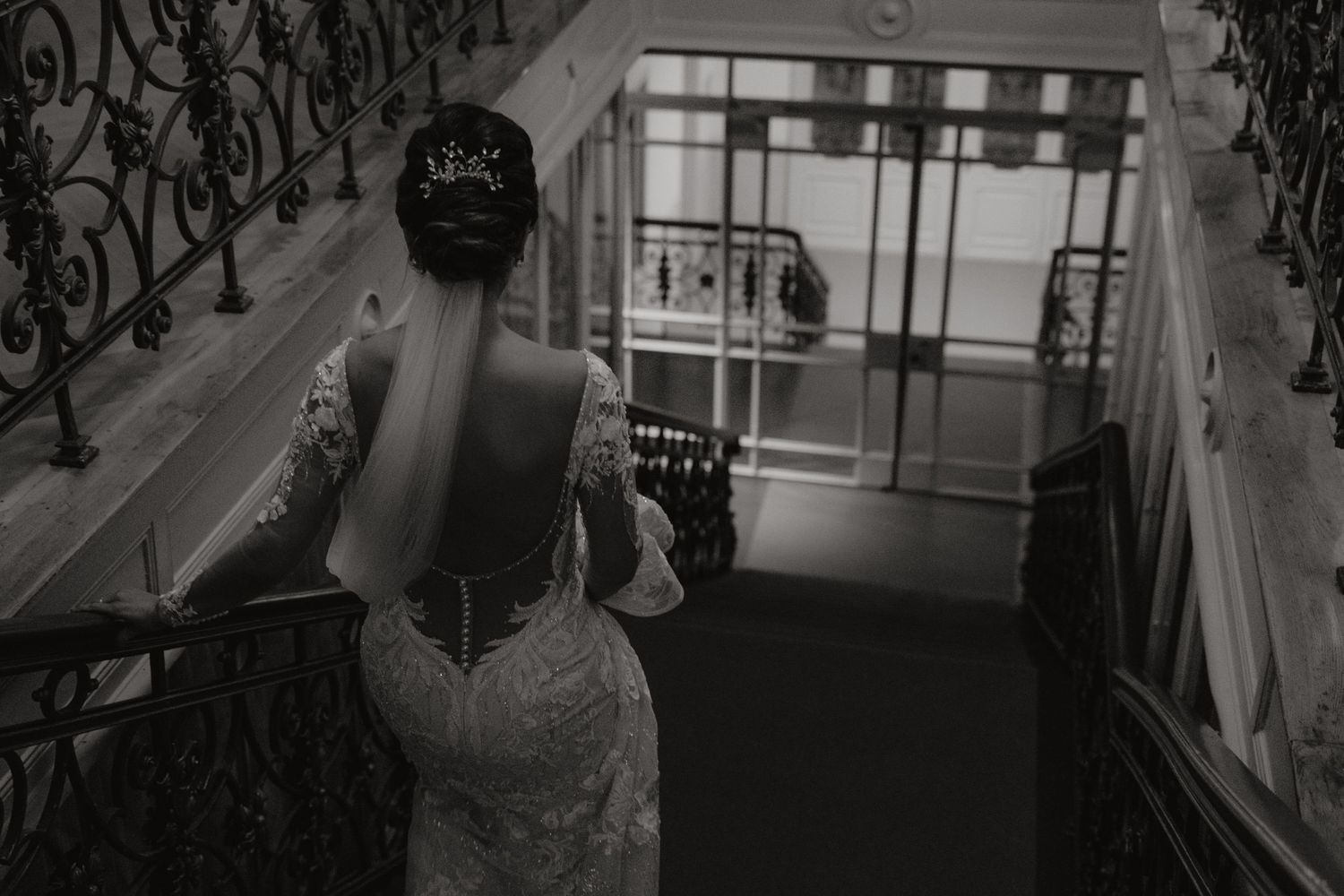 Back view of a bride in a fitted lace wedding dress walking down ornate stairs.