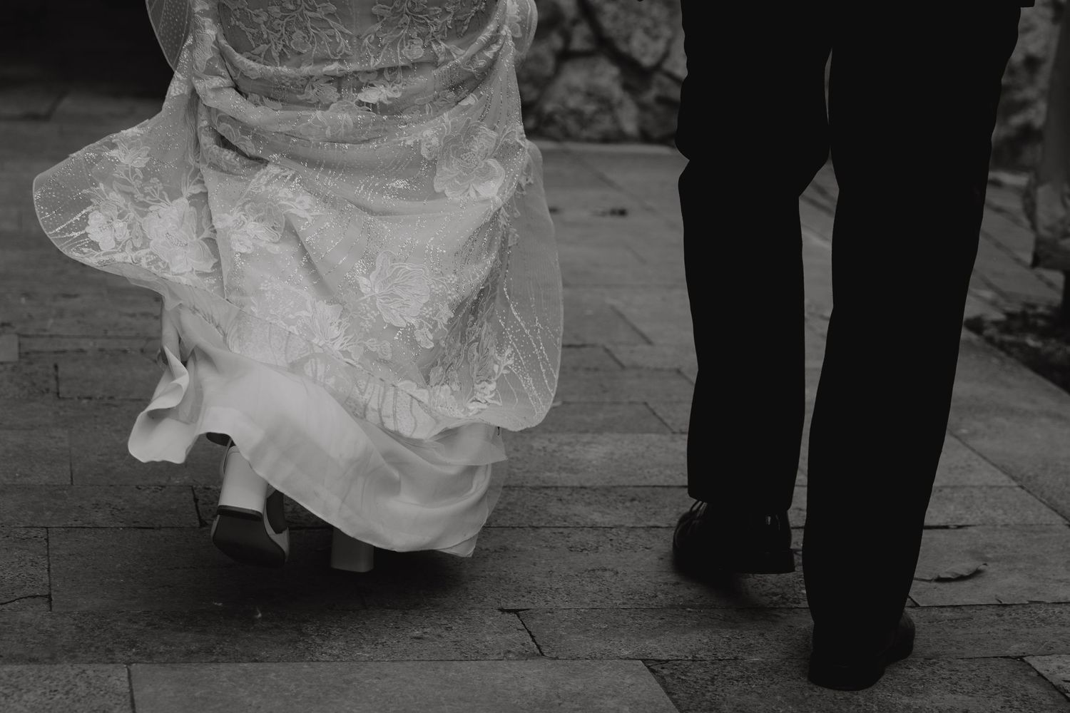 Black and white detail shot of bride and groom's feet dancing on wooden floor.