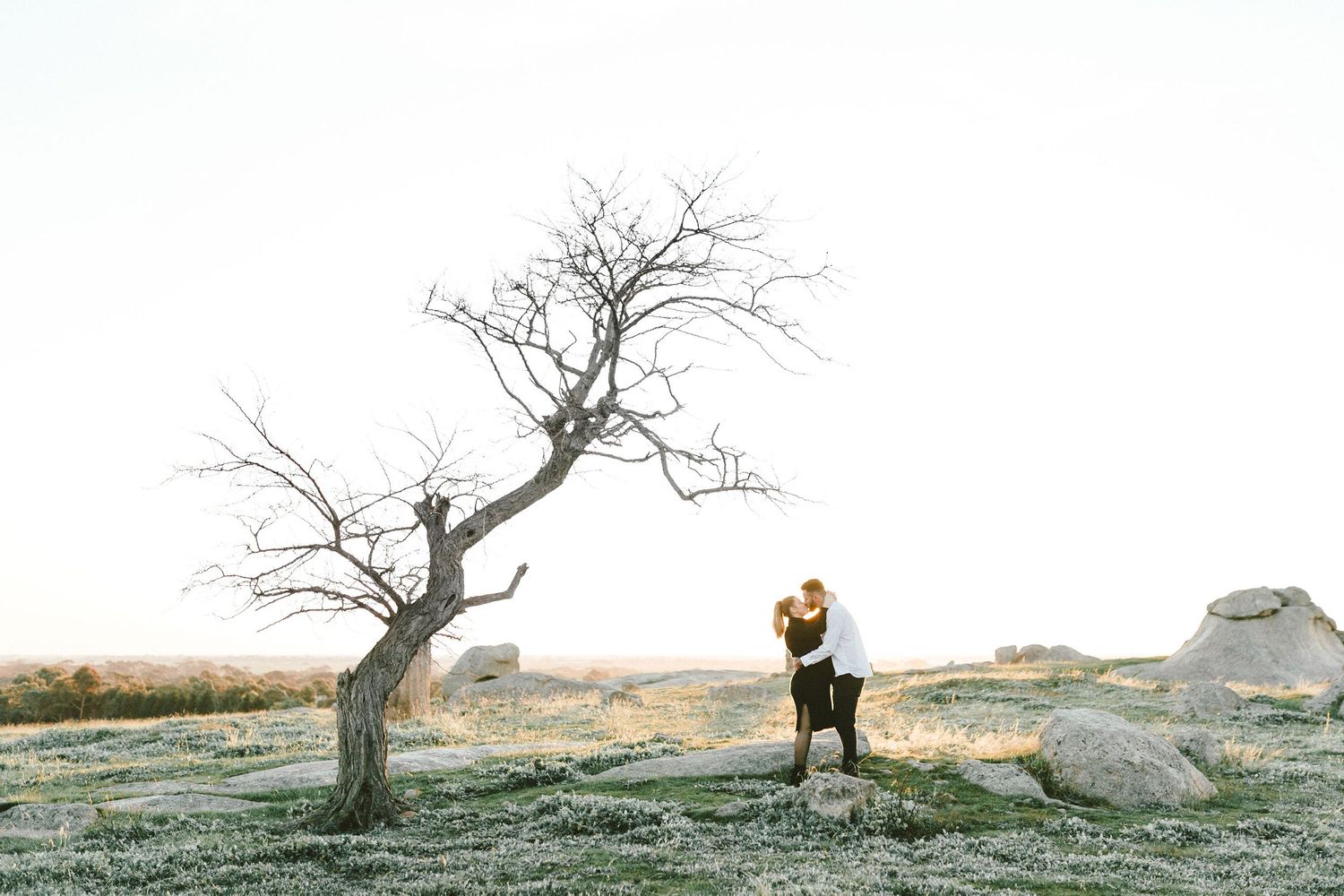 Two figures walk along a rocky hilltop against a scenic landscape at golden hour.