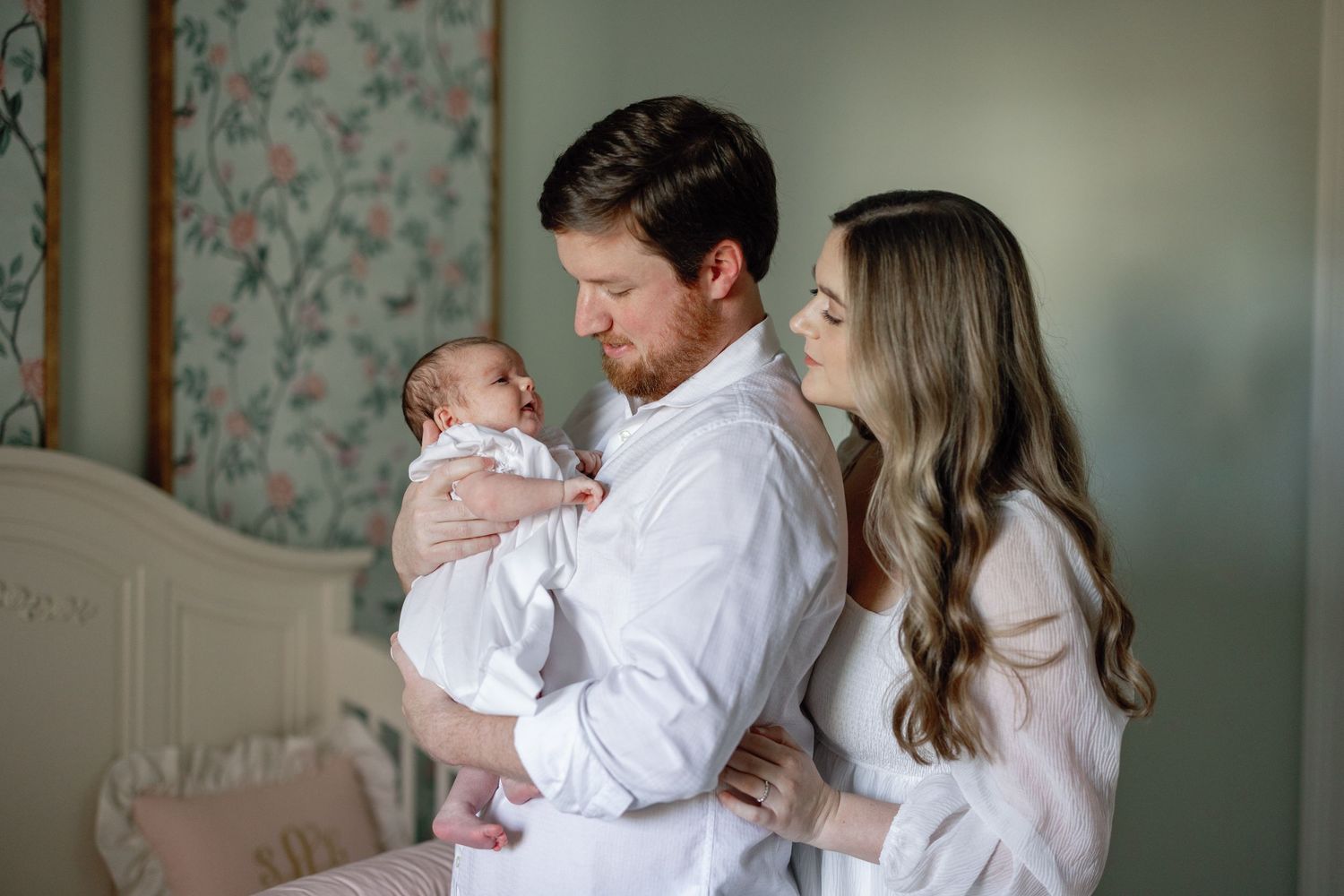 A tender family moment in a nursery room with floral wallpaper.