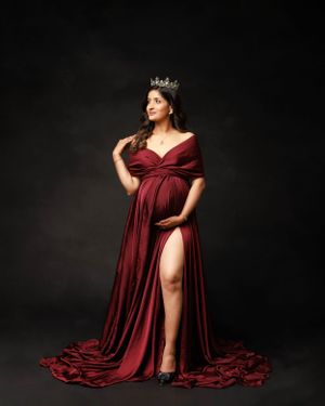 Regal maternity portrait in burgundy gown with crown and dramatic side slit.