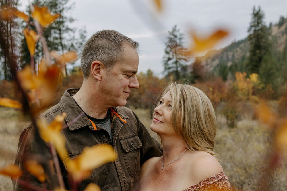 Romantic couple embraces in autumn forest setting with golden leaves falling around them.