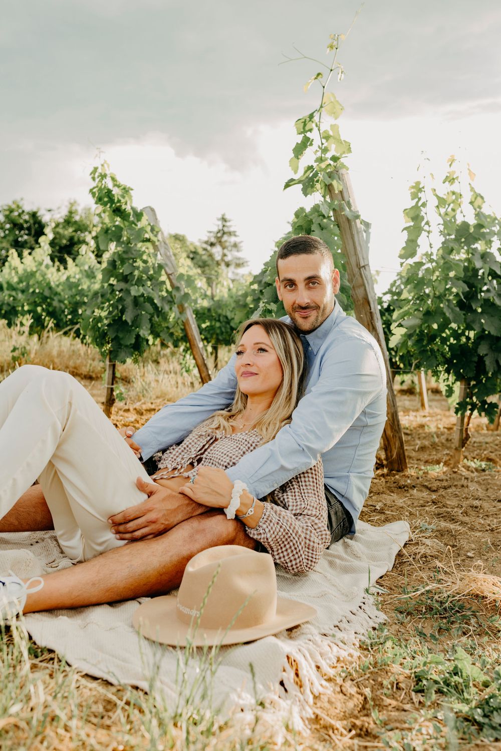 Couple relaxing on picnic blanket in sunny vineyard, sharing intimate moment.