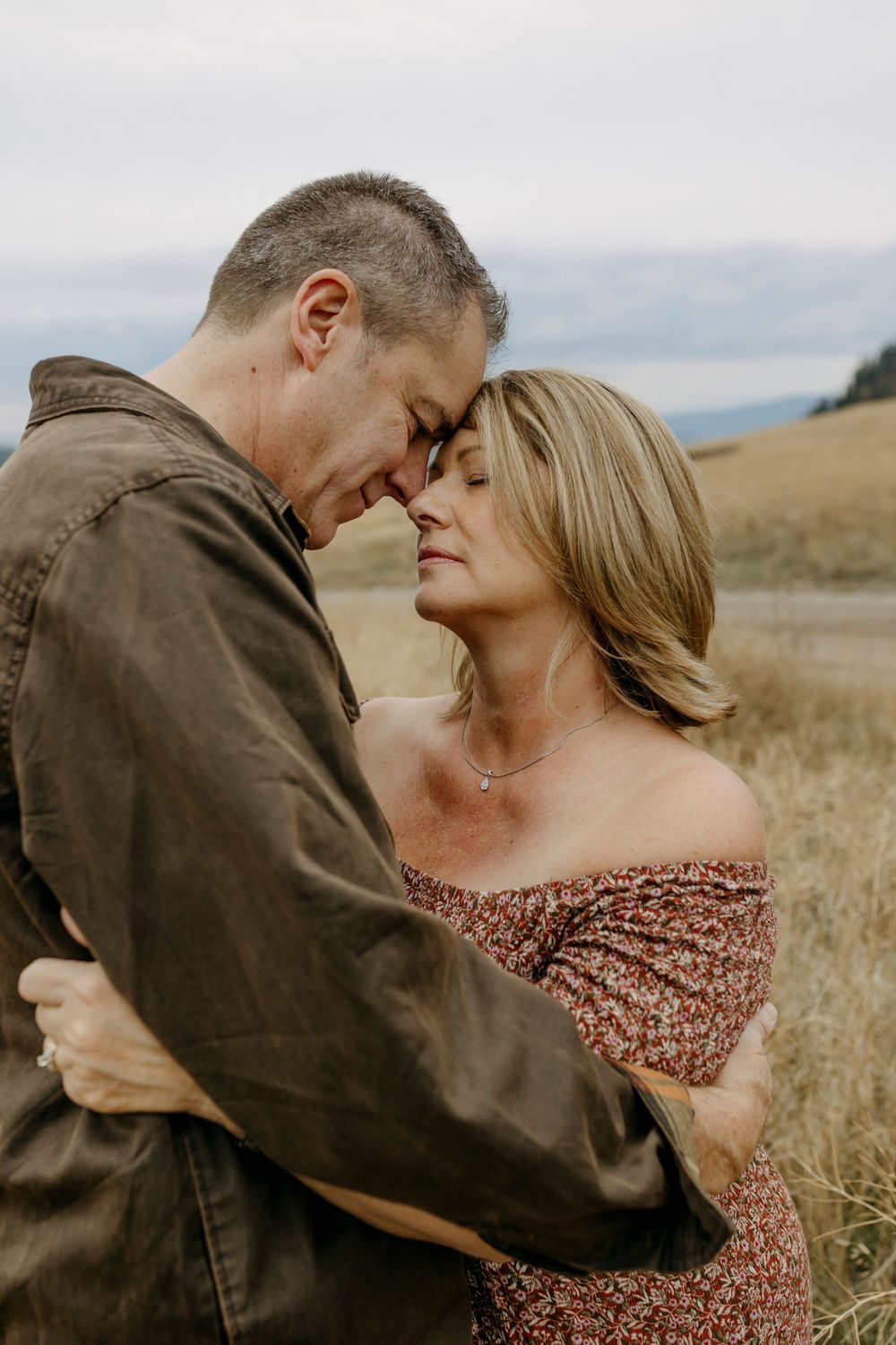 Romantic couple embracing in golden field during sunset with mountains in background.