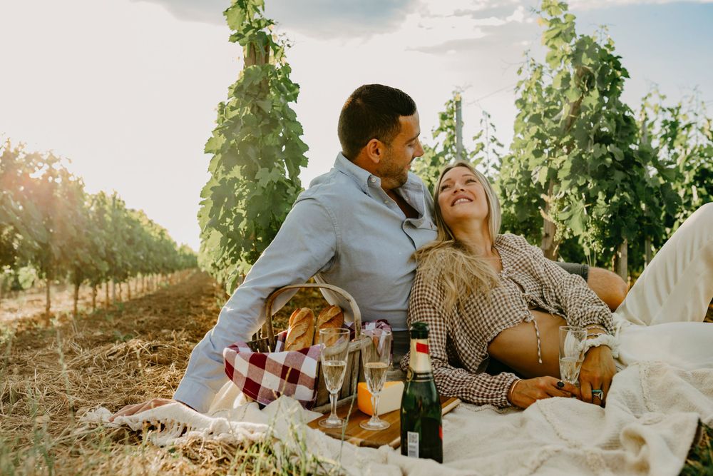 Romantic couple enjoying wine during sunset picnic in vineyard setting.