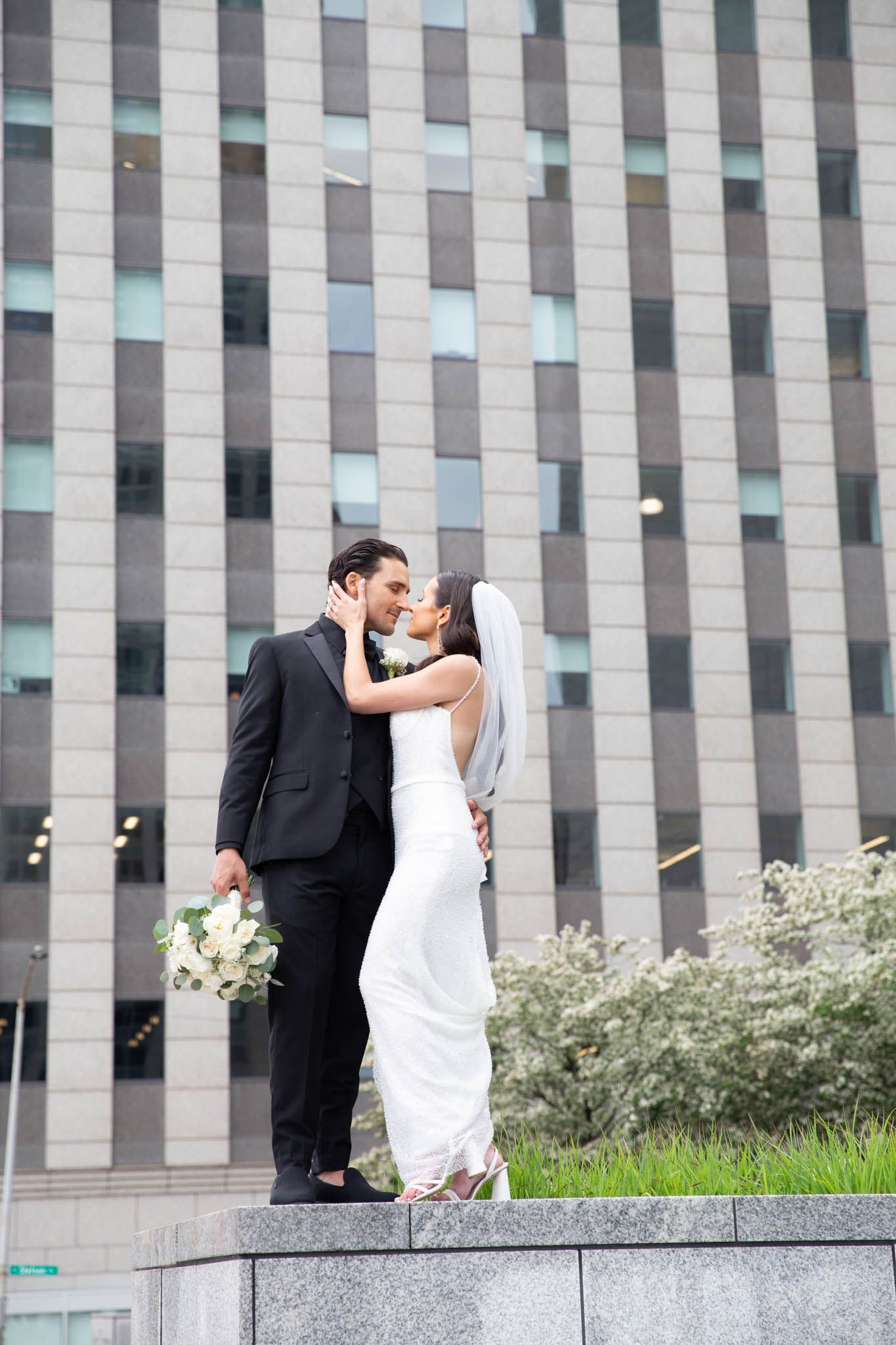 A romantic wedding portrait with couple kissing against a modern architectural backdrop.