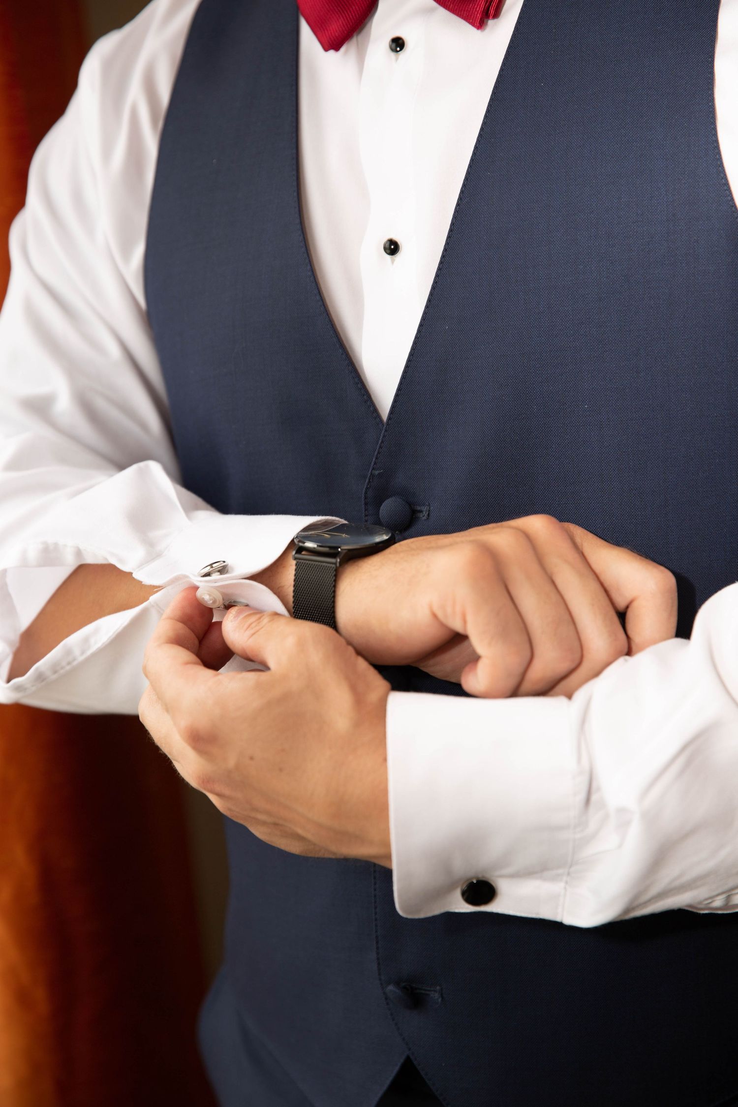 Close-up of formal attire showing navy vest, red bowtie, and hands adjusting a smart watch.