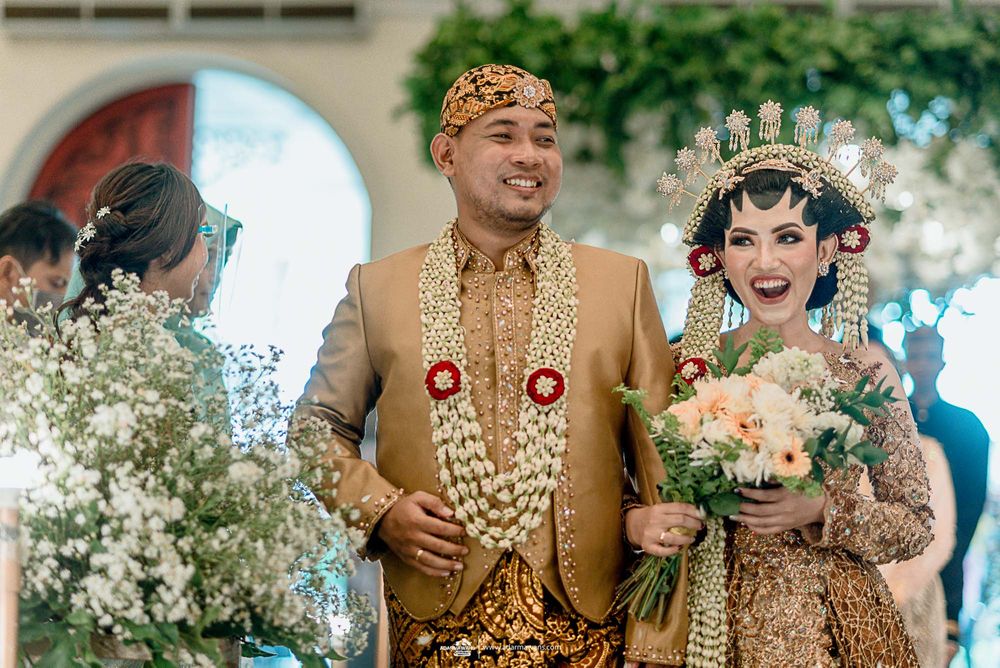 Wedding couple wearing ornate traditional Indonesian wedding attire with gold details and floral bouquet.