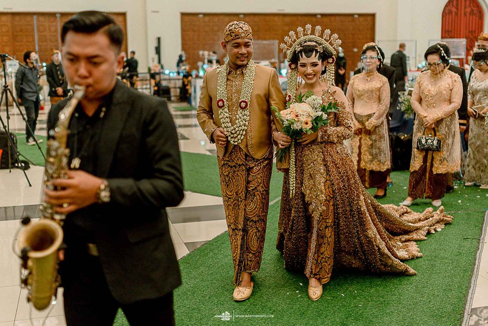 Wedding procession on green carpet with live saxophone music and traditional Indonesian formal wear.