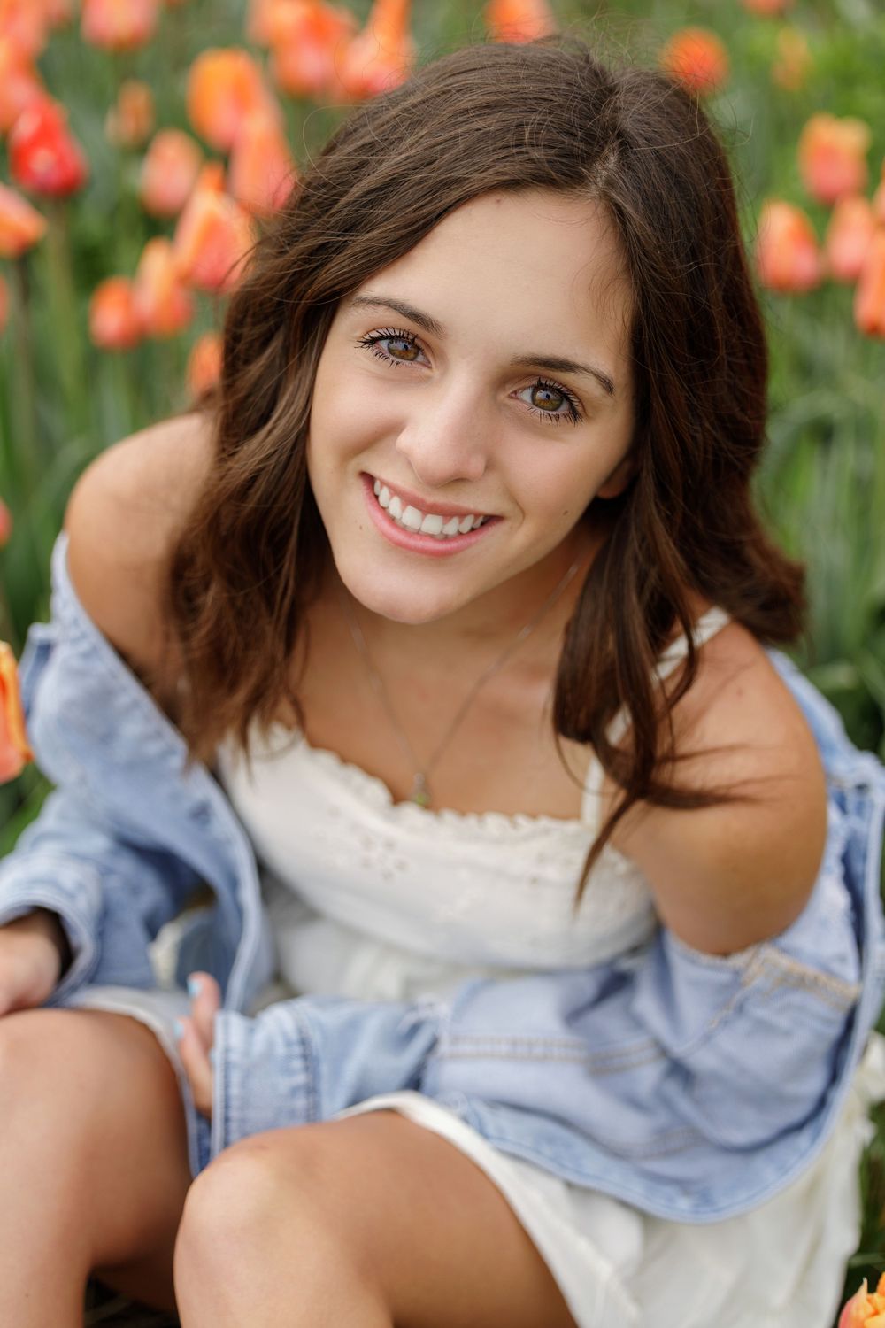 Portrait in a garden of orange tulips wearing denim jacket and white dress.