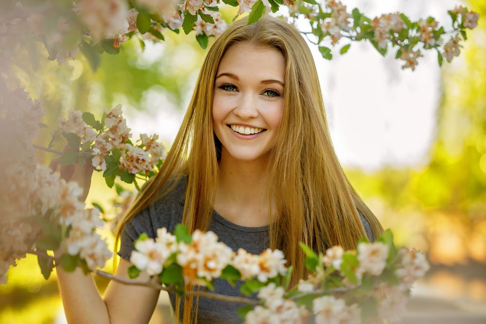 Spring portrait surrounded by blossoming apple tree branches in soft natural lighting.