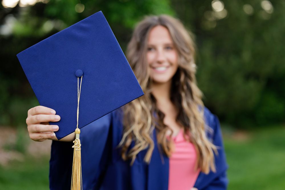 Graduation photo showing a blue cap with tassel against a blurred green background.