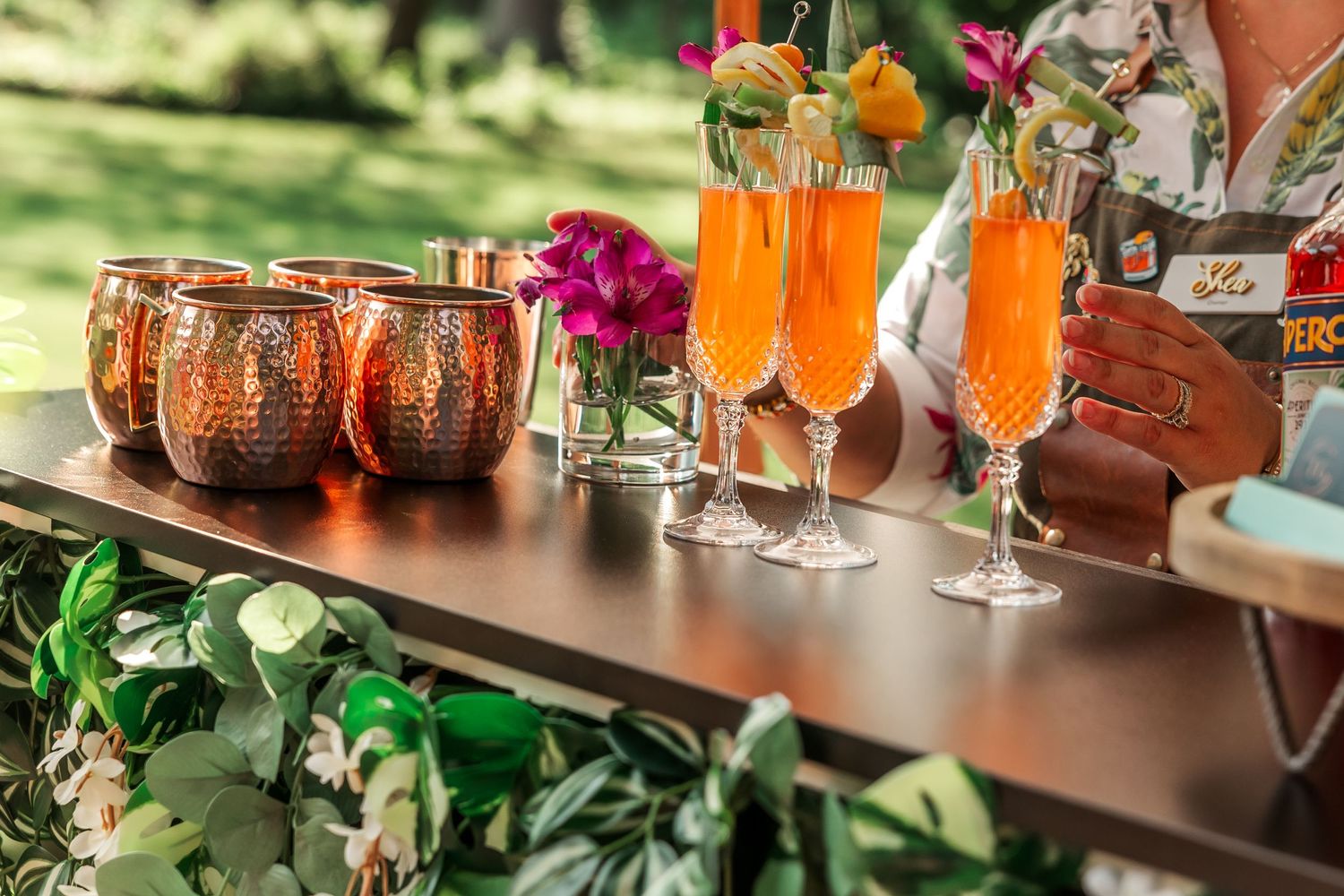 Copper Moscow mule mugs and orange cocktails arranged on decorated bar with fresh flowers.