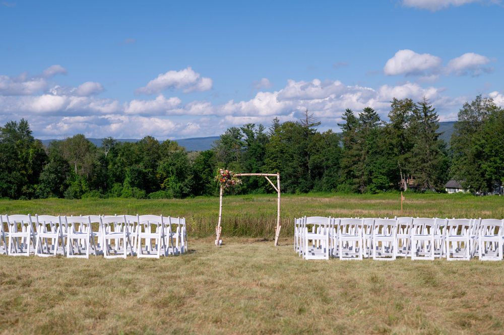 White chairs arranged for an outdoor wedding ceremony with mountains and forest in the background.