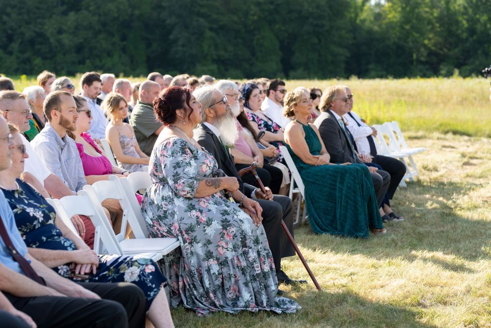 Wedding guests seated in white chairs at outdoor countryside ceremony.