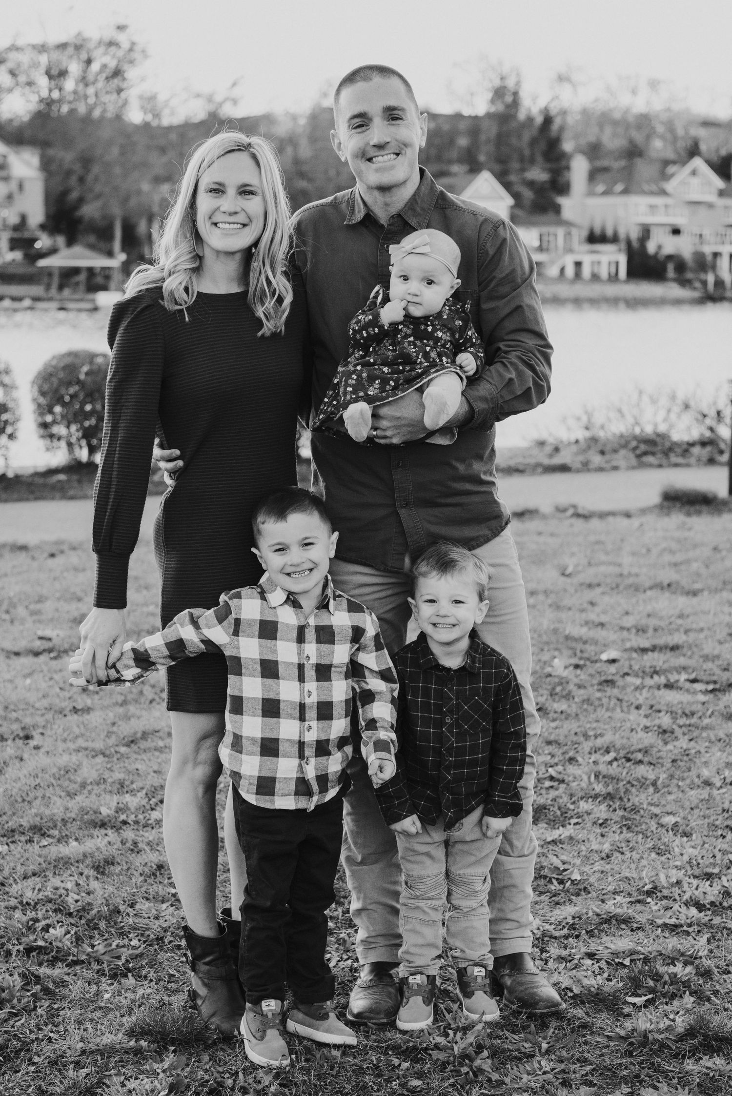 Black and white outdoor family portrait with waterfront view in background.