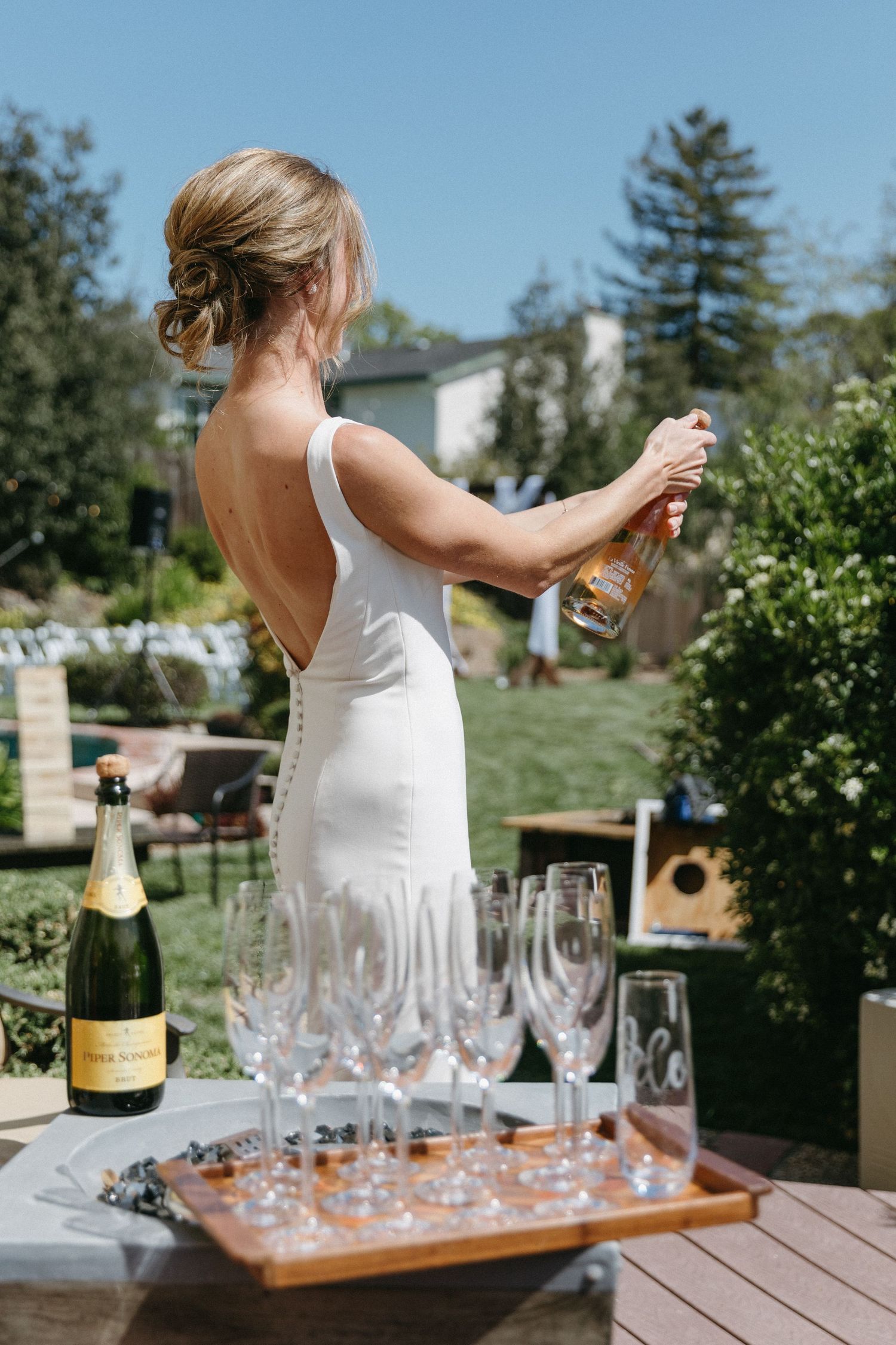 Woman in white dress pouring champagne outdoors on a sunny summer day.