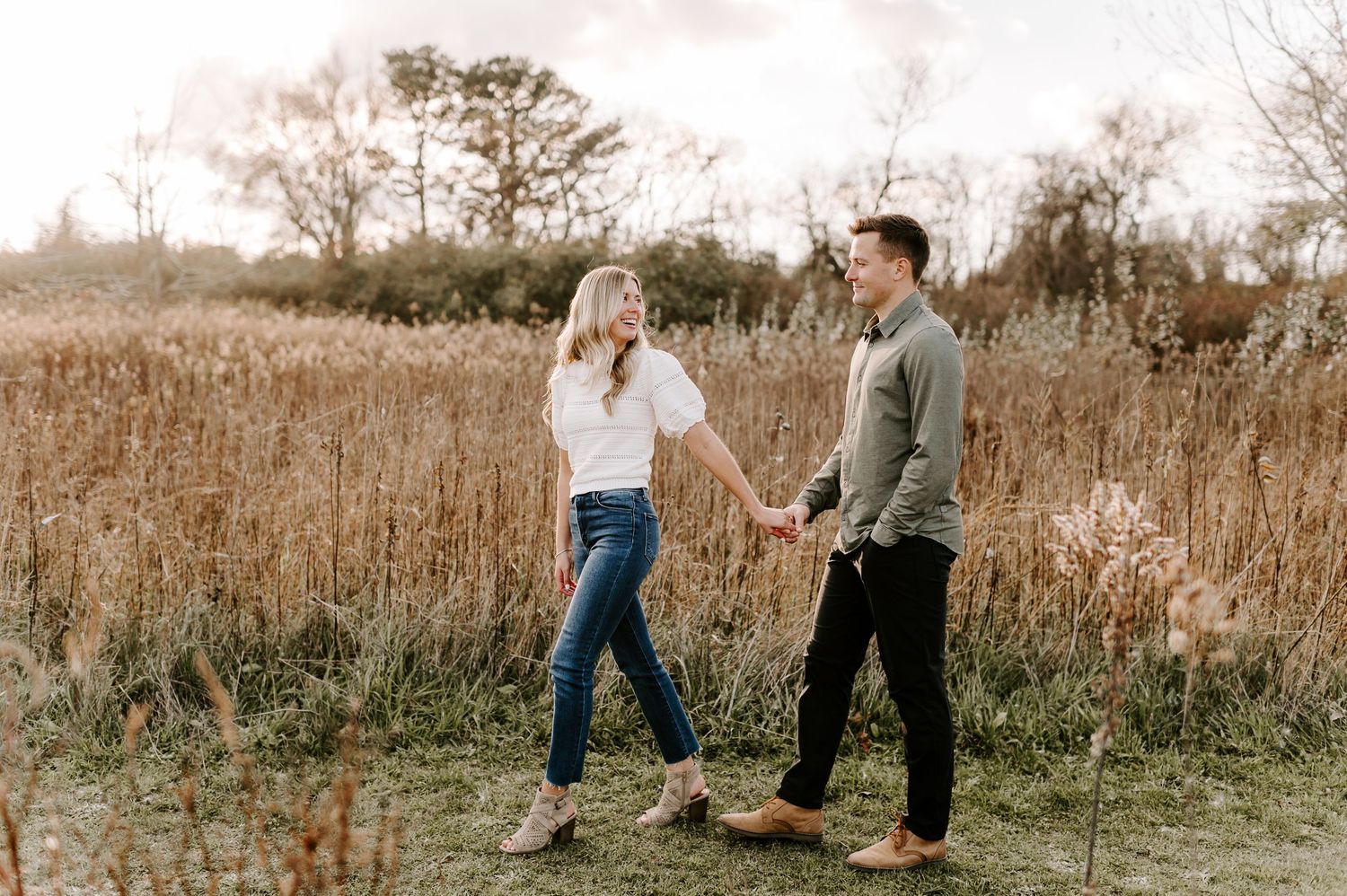 Couple walking together through tall grass in golden autumn field.
