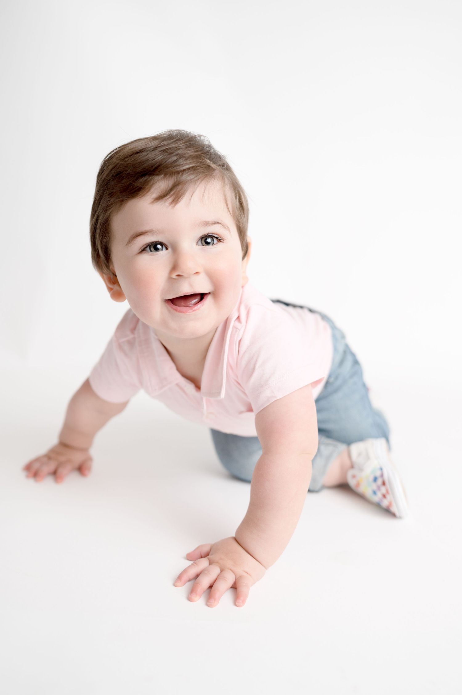 Baby in pink shirt and jeans crawls on white background showing happy expressions.