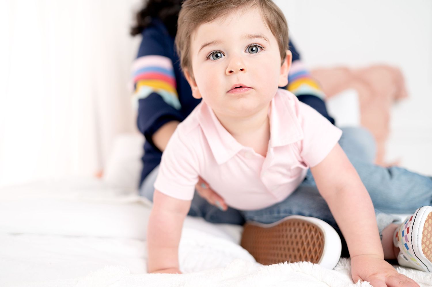 Baby in pink outfit crawls and explores on white seamless background.