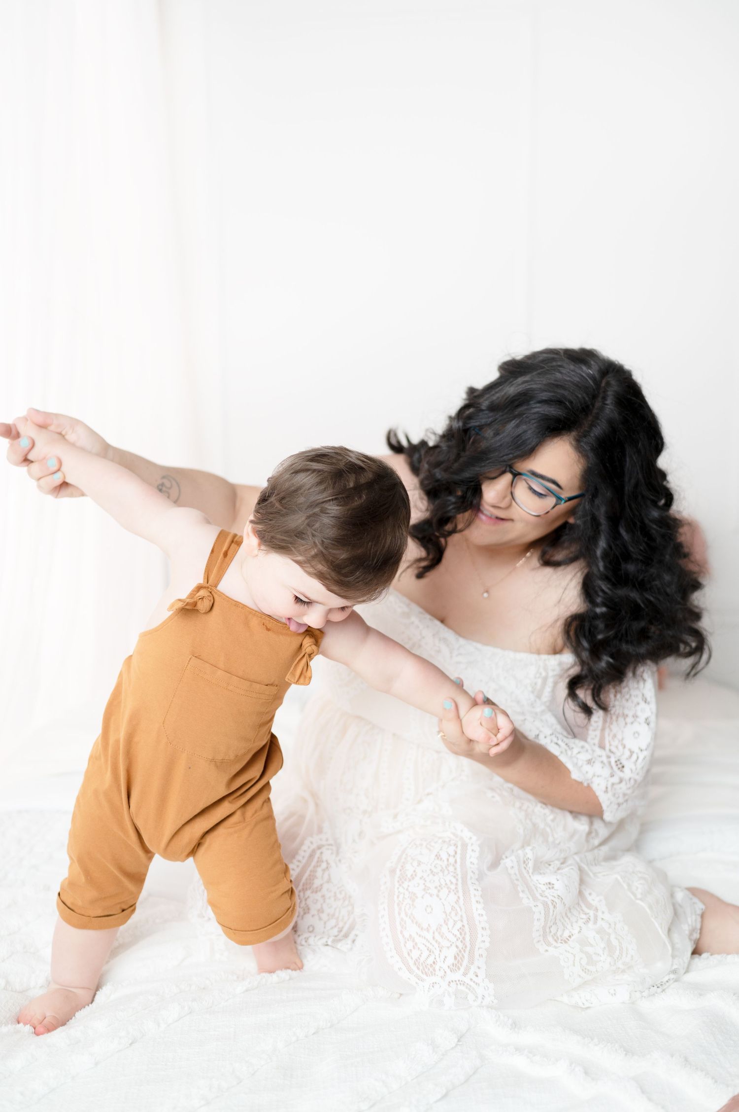 Playful moment between parent and toddler in orange overalls on white background.