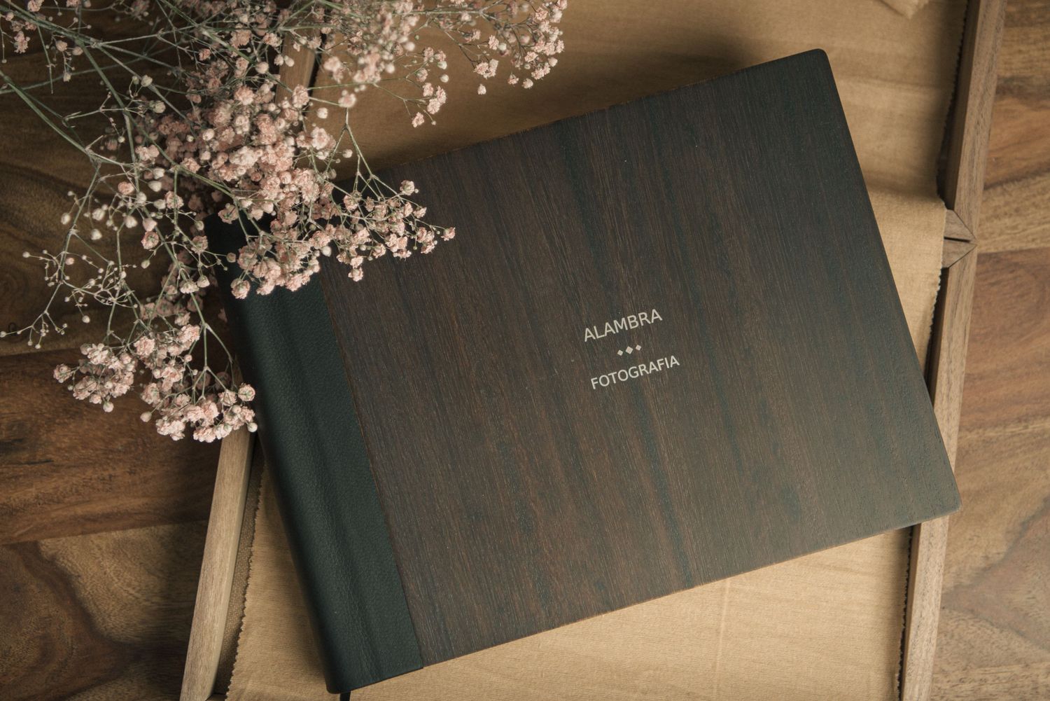 Un album fotografico di nozze si trova su una superficie di legno accanto a delicati fiori rosa.