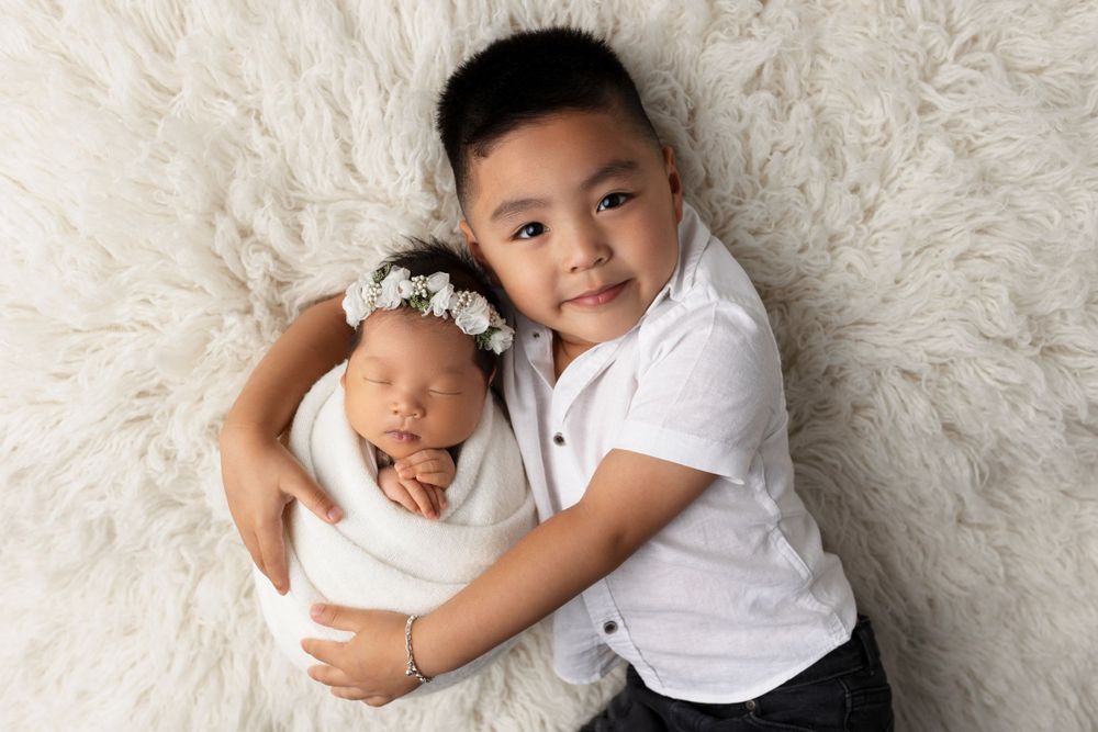 Sweet portrait of siblings embracing on soft white fur background.