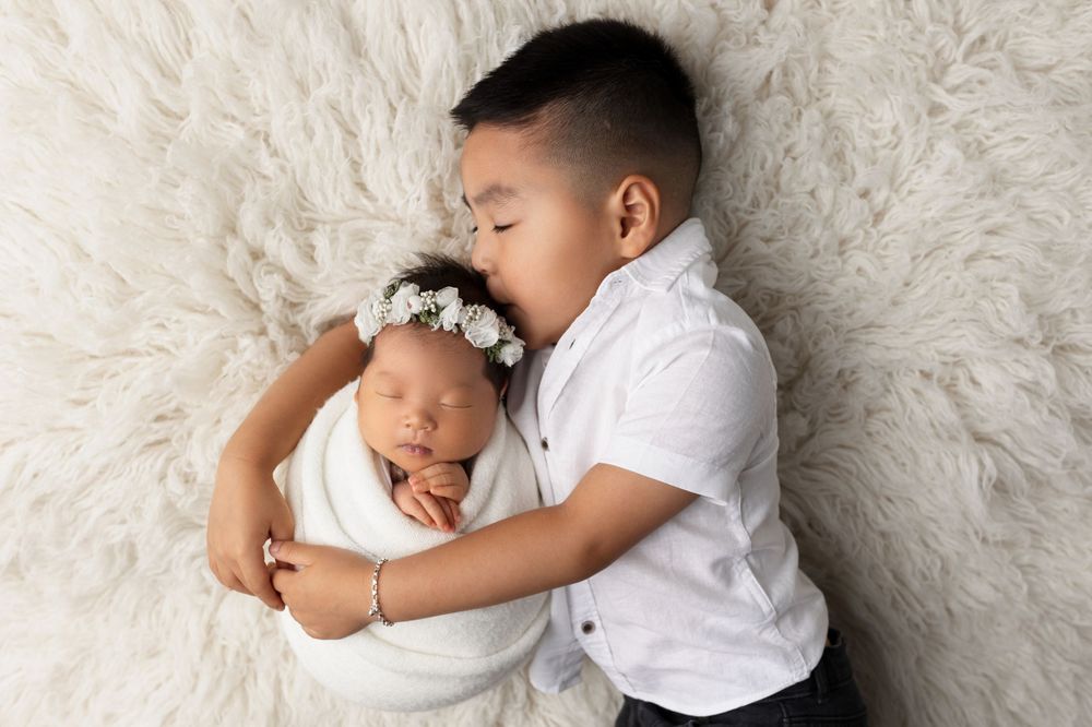 Siblings sharing tender moment on white fluffy rug during portrait session.