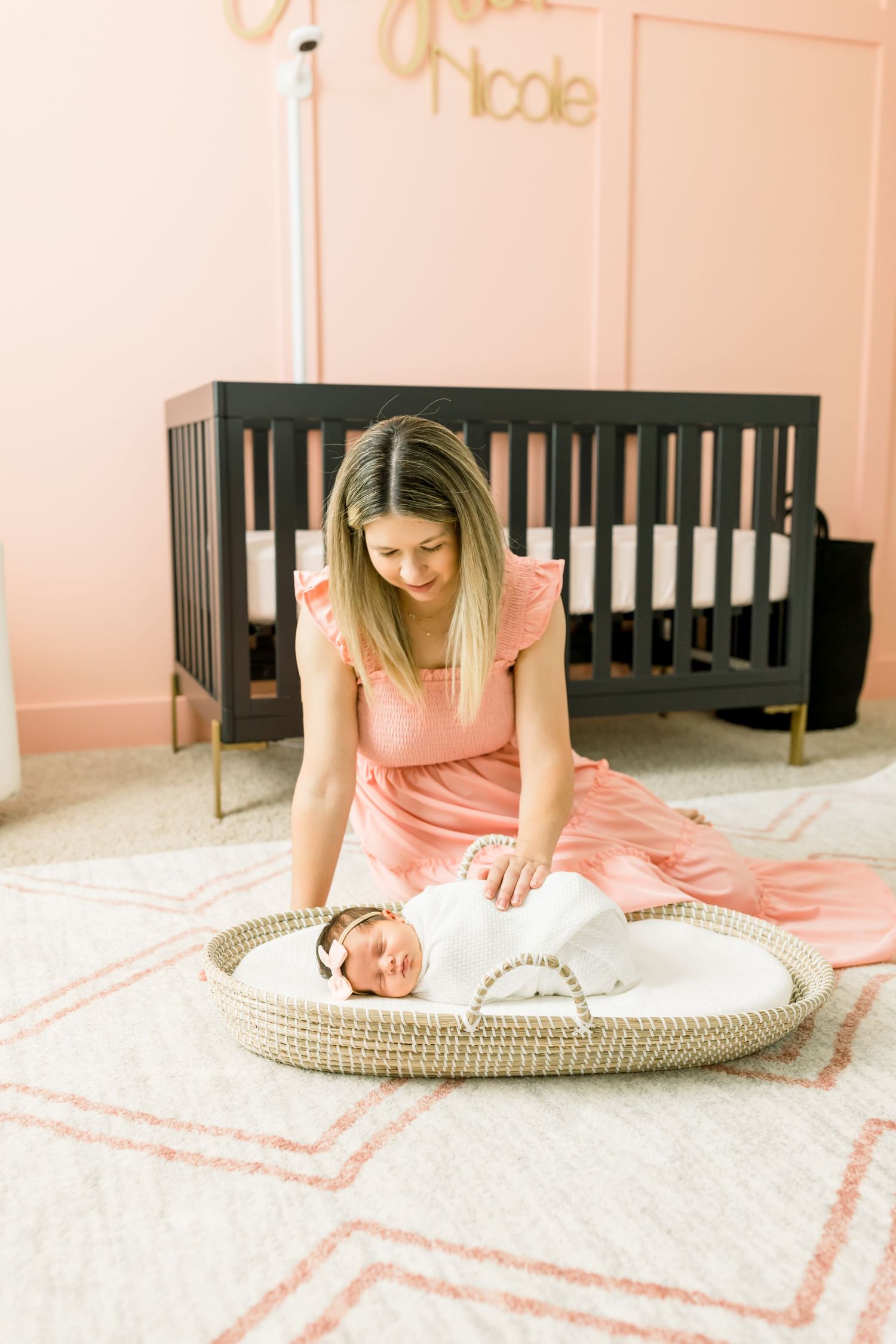 Nursery scene with dark crib and person in pink dress tending to baby in woven basket.
