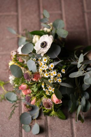 Rustic wedding bouquet featuring anemones, eucalyptus, and wildflowers on brick surface.