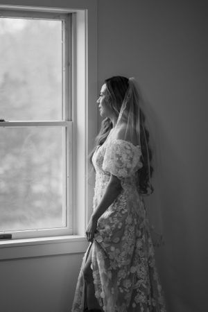 Artistic black and white bridal portrait by window with lace dress and veil.
