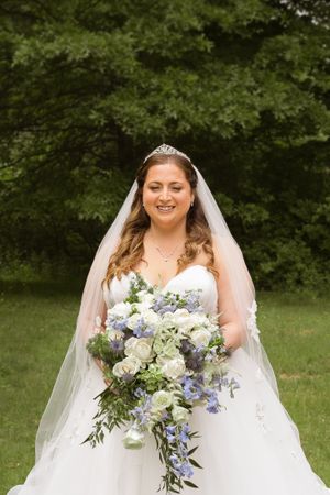 Bride with cascading blue and white bouquet poses in garden setting.