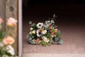 A delicate floral arrangement with white anemones, roses, and eucalyptus sits on a dusty brick surface.