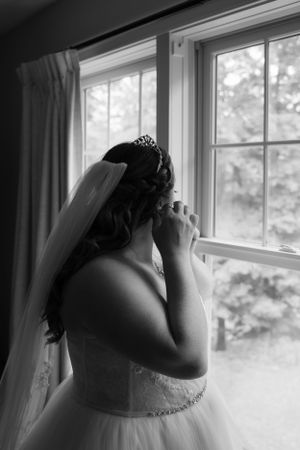 A dreamy black and white wedding photo showing a bride in a tulle gown near a sunlit window.