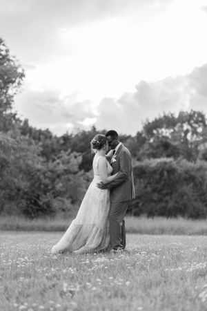 A black and white portrait of a couple embracing in a wildflower meadow.
