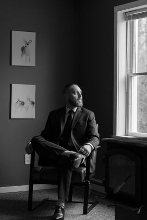 Artistic black and white portrait in formal attire near window with framed artwork.