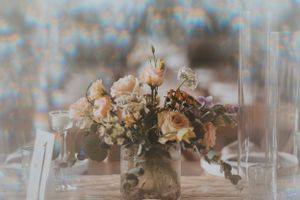 Soft peachy roses and delicate flowers arranged in a vintage vase on a light colored table setting.