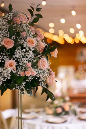 Elegant wedding centerpiece with pink roses and baby's breath against soft bokeh lights.
