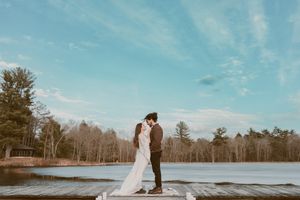 Romantic winter wedding photo of couple standing on dock overlooking frozen lake.