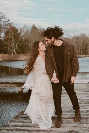 Candid moment of couple laughing together on lakeside dock during wedding photoshoot.