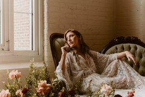 An elegant vintage-inspired portrait on a tufted chaise with roses and soft window light.