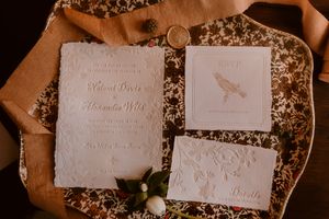 Elegant white wedding invitations with floral design displayed on textured copper background.