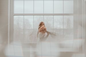 A dreamy silhouette of a person in white holding flowers by a sunlit window.