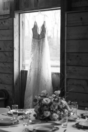 Wedding dress displayed in rustic barn window with table setting in foreground.