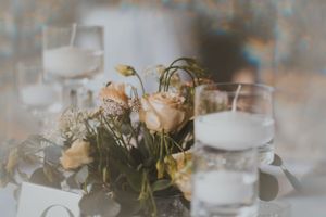 Soft focus table centerpiece with peach roses and drinking glasses.