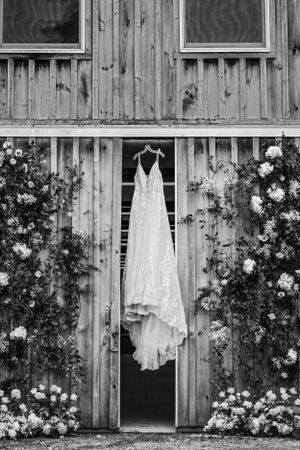 A white lace wedding dress hangs between rustic wooden doors surrounded by climbing roses.