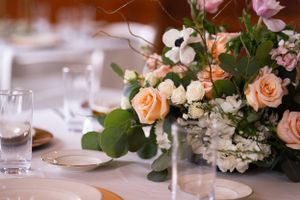 Romantic table setting with peach roses and white floral centerpiece at wedding reception.
