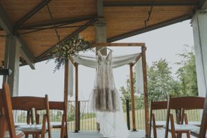 Wedding dress hangs from wooden arch structure in rustic indoor venue.