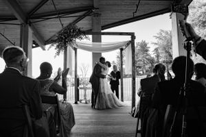 A black and white photo of a wedding ceremony under a decorated outdoor pavilion with guests watching.