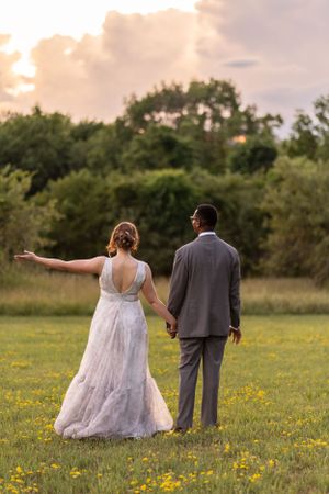 A couple in wedding attire stands in a wildflower field during sunset.